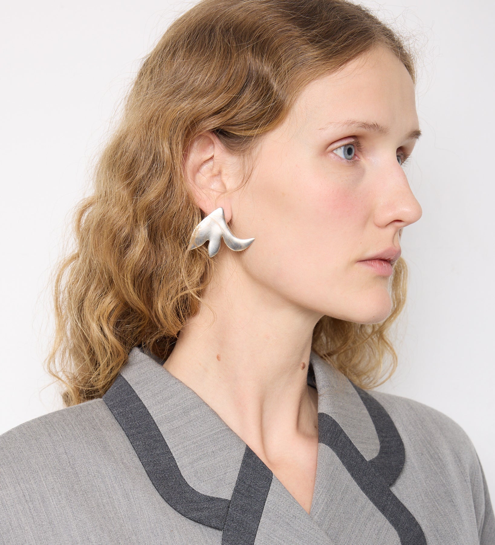 Model wears the Mono Earring Wisley Pink by Mann Studio – a sculptural silver-tone single earring with a bold, organic shape.