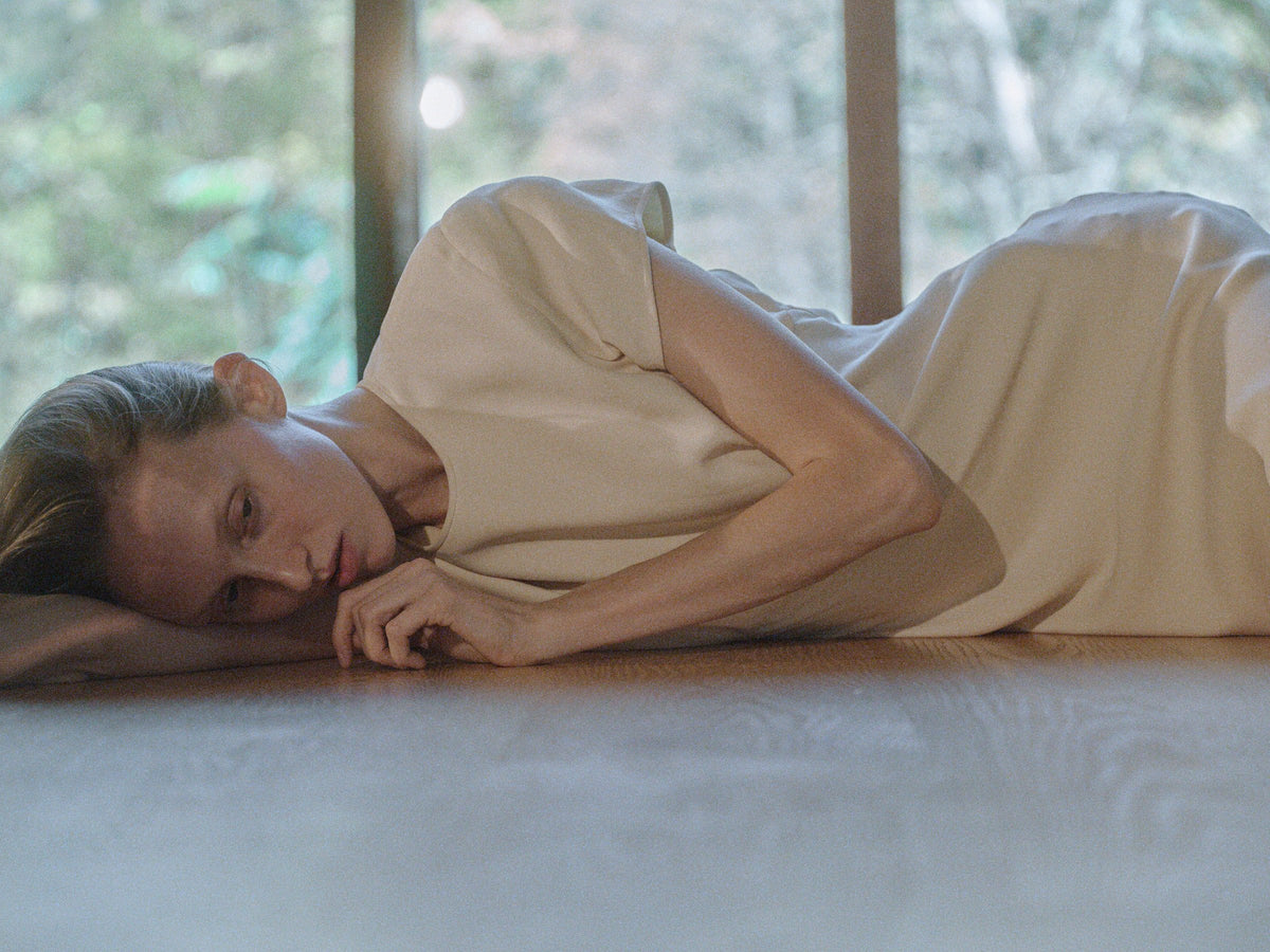 Woman reclining beside a window in a cream vintage dress